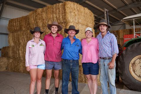 Curtis family stands in front of stack of hay bales