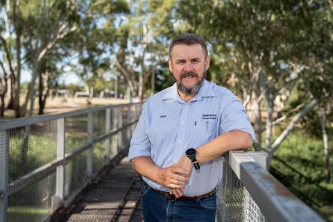 Regional Area Manager, Terry Pulsford is standing on a bridge, leaning on the rail with a green park behind him.